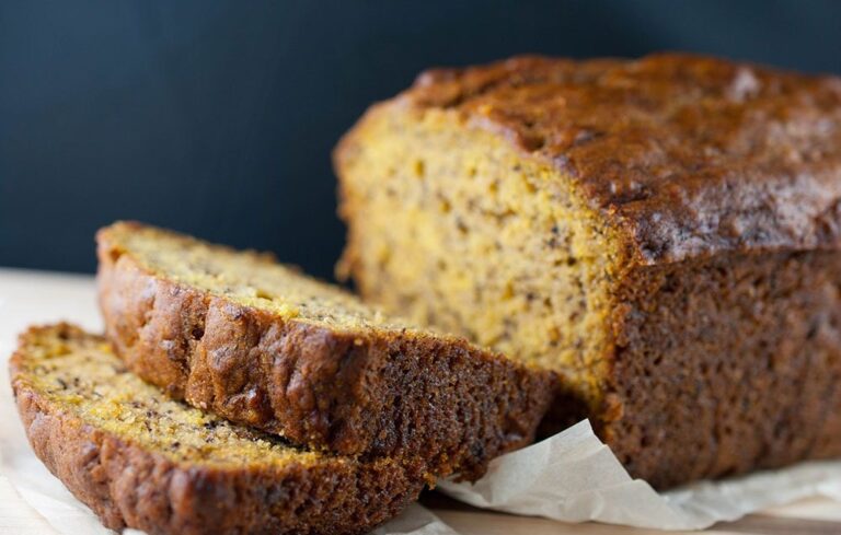 A moist and freshly baked pumpkin banana loaf sliced to reveal its soft and golden texture, resting on parchment paper.