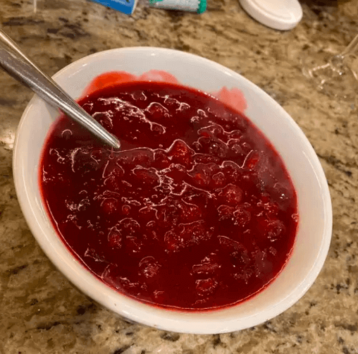 A bowl of freshly made whole berry cranberry sauce, vibrant red with visible whole cranberries, placed on a granite countertop.