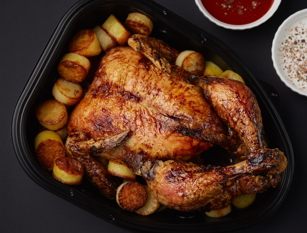 Golden-brown roasted turkey surrounded by crispy roasted potatoes in a black serving tray.