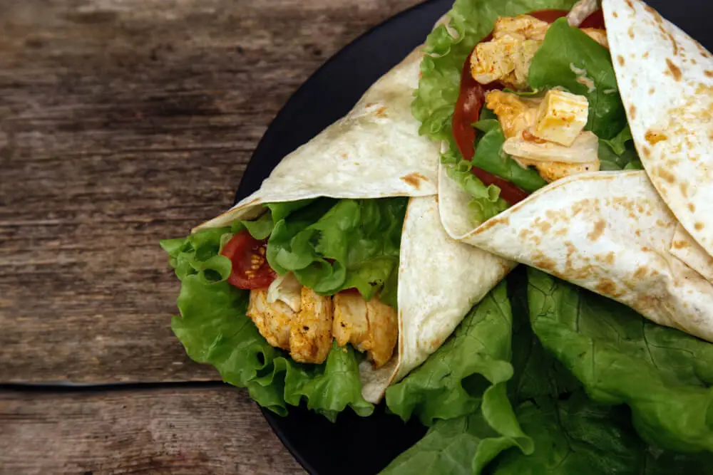 Fresh Chicken Caesar Wraps on a dark plate with crisp lettuce, grilled chicken, and tomatoes on a rustic wooden background.