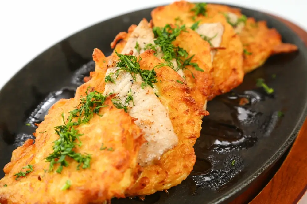 Crispy golden potato pancakes garnished with fresh herbs, served on a black plate.