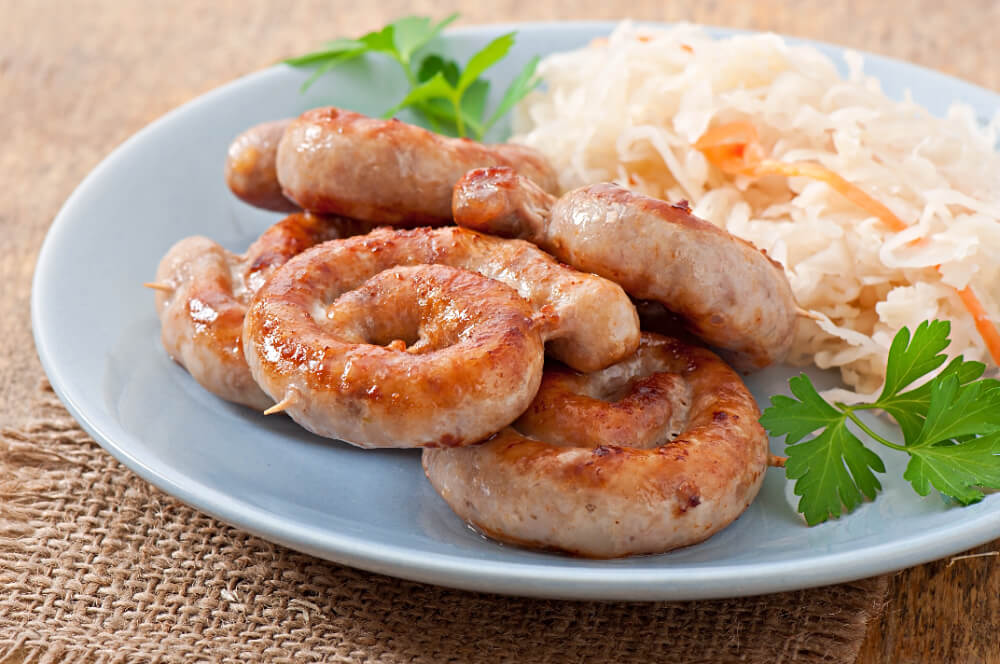 Coiled grilled sausages served on a plate with sauerkraut and fresh parsley garnish, perfect for a traditional meal.