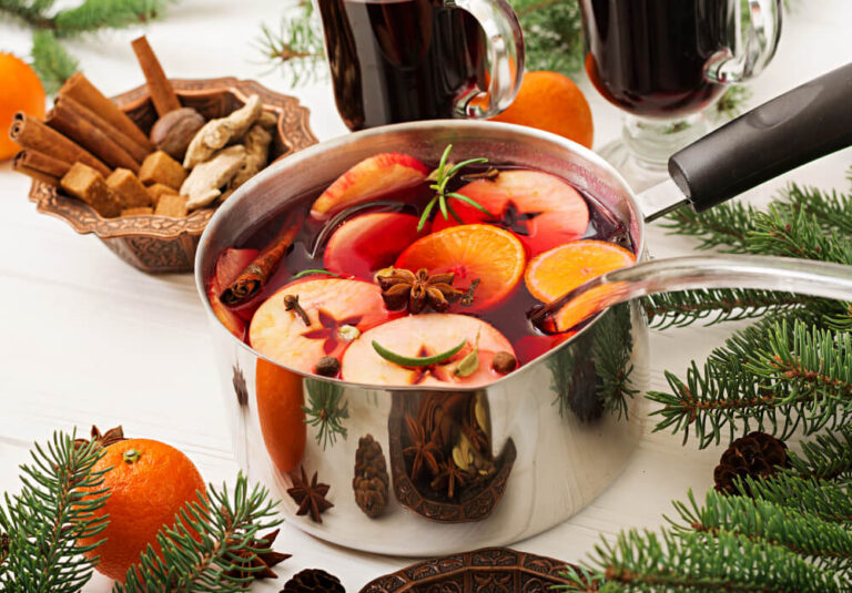 A pot of non-alcoholic Christmas punch with orange slices, apples, cinnamon sticks, and star anise, surrounded by festive decorations.