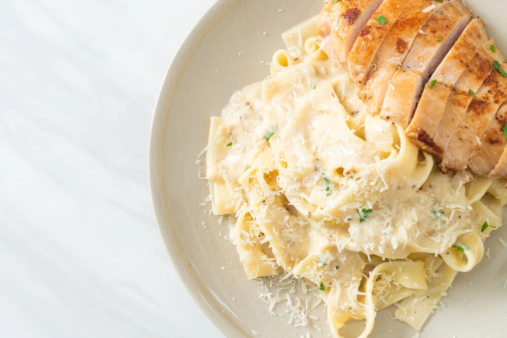 Sliced grilled chicken breast served on a bed of creamy fettuccine carbonara garnished with Parmesan and parsley.