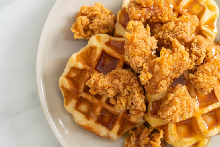 Crispy fried chicken pieces on golden waffles drizzled with syrup, served on a white plate.