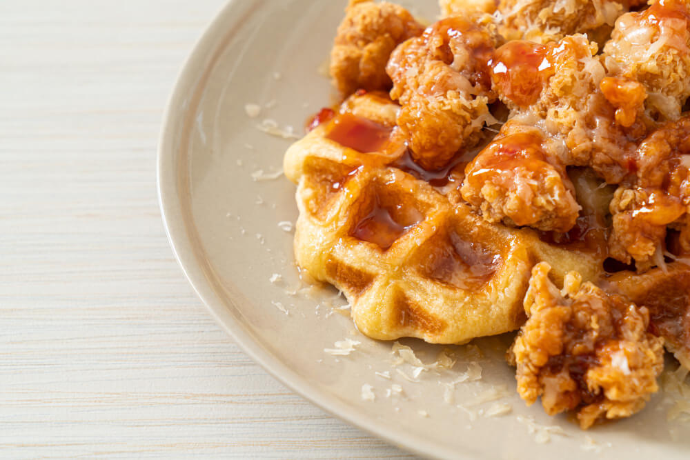 Golden waffles topped with crispy fried chicken, drizzled with syrup, and sprinkled with shredded cheese.