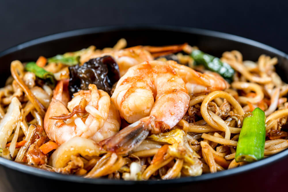 A bowl of stir-fried shrimp chow mein with thick noodles, vegetables, and plump prawns.