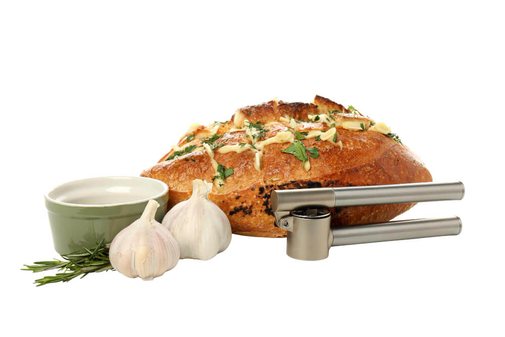 Pull apart garlic bread loaf with melted butter, fresh herbs, garlic cloves, a garlic press, and a ceramic dipping bowl.