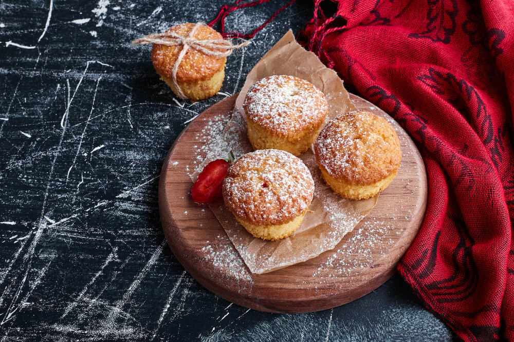 Three French Breakfast Puffs dusted with powdered sugar, served on a wooden board with a red napkin and sliced strawberry garnish