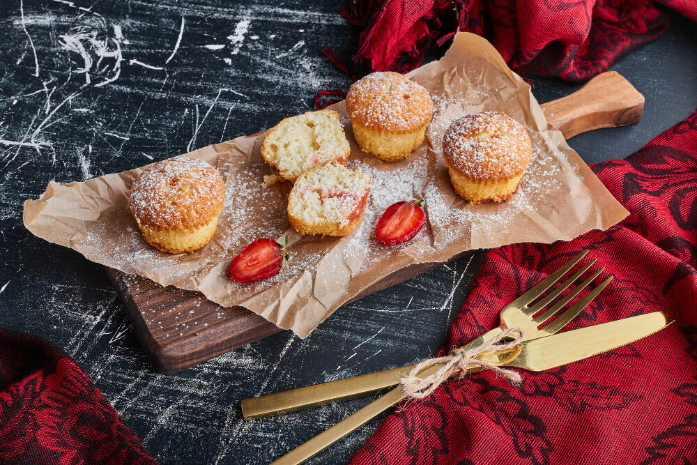 French Breakfast Puffs on a wooden serving board, sprinkled with powdered sugar, paired with strawberries, and styled with a rustic red napkin and gold cutlery.