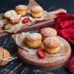 Freshly baked French Breakfast Puffs sprinkled with powdered sugar and garnished with strawberries on wooden serving boards.