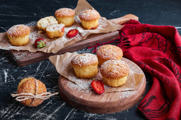 Freshly baked French Breakfast Puffs sprinkled with powdered sugar and garnished with strawberries on wooden serving boards.