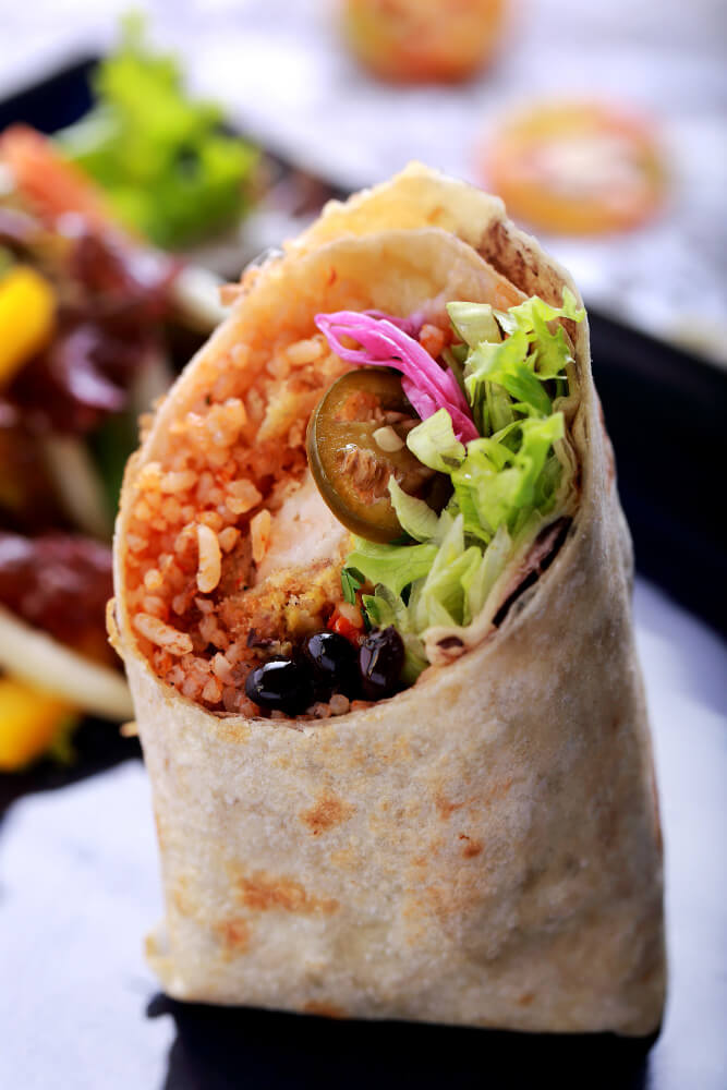 Close-up of a breakfast burrito filled with rice, black beans, lettuce, jalapeños, and pickled onions wrapped in a tortilla.