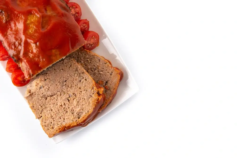 Top-down view of a sliced meatloaf with a tomato glaze, served on a white plate with cherry tomato garnish against a white background.