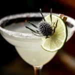 A close-up of a classic Margarita served in a wide-brimmed glass with a salted rim, garnished with a lime wheel and a decorative floral element.