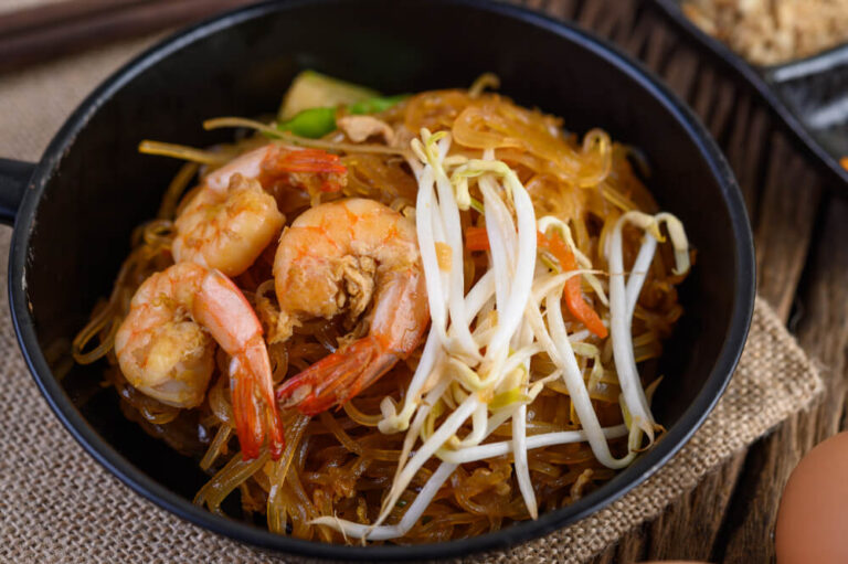 A bowl of shrimp chow mein topped with bean sprouts, featuring stir-fried noodles, prawns, and vegetables.