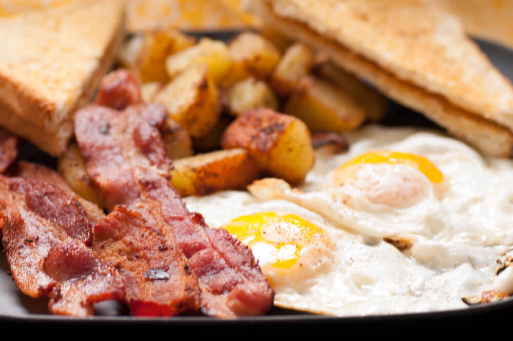 Crispy bacon, two fried eggs, golden potatoes, and buttered toast on a breakfast plate.