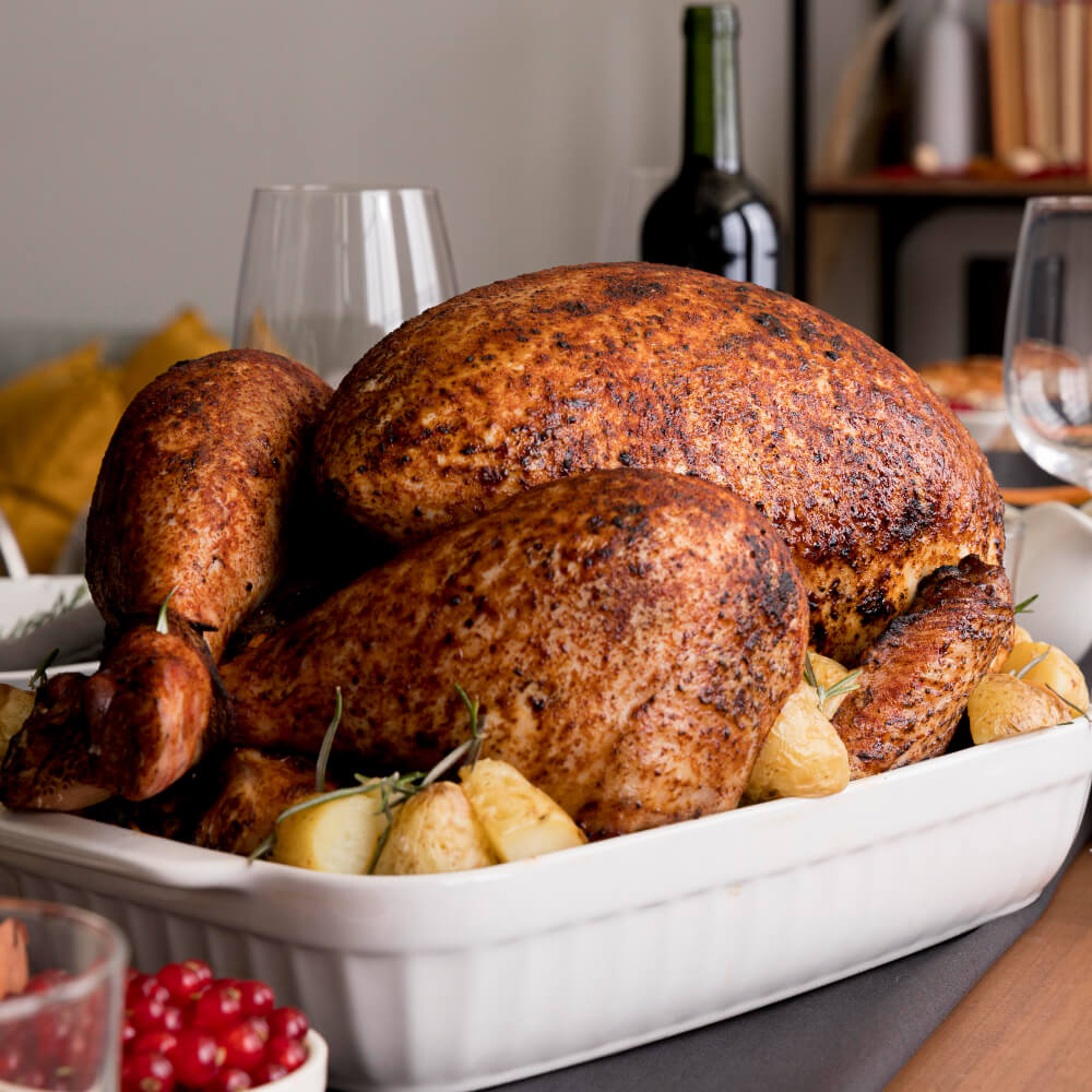 Perfectly roasted turkey served in a white dish, surrounded by golden potatoes and fresh rosemary, on a festive dinner table.