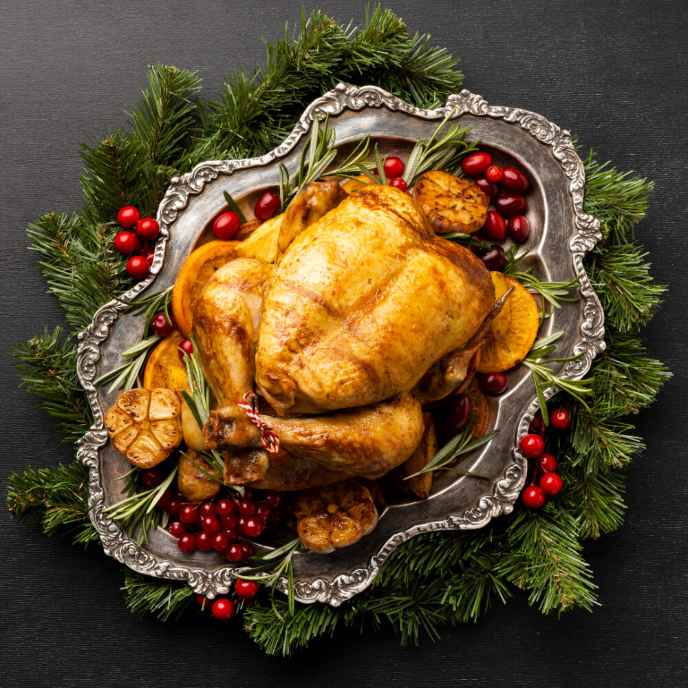 Golden roasted turkey on a decorative silver platter surrounded by festive greenery and cranberries.