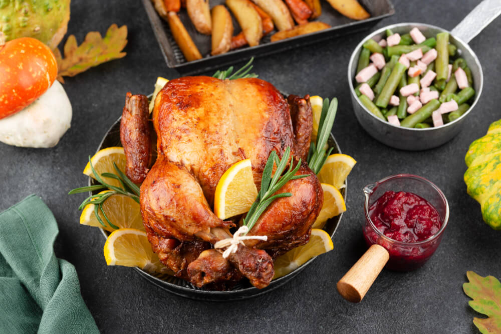 A golden roasted turkey garnished with lemon slices and rosemary, served with cranberry sauce, green beans, and roasted vegetables.