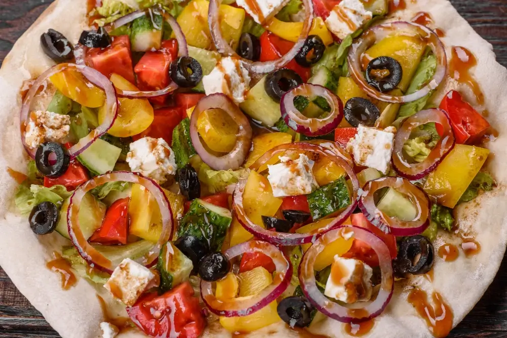 Fresh veggie pizza with colorful toppings including tomatoes, bell peppers, red onions, black olives, and feta cheese on a crispy crust.