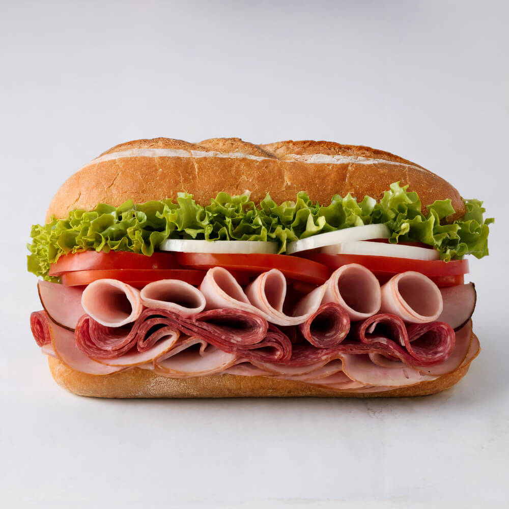 A freshly made sandwich featuring layers of deli meats, lettuce, tomatoes, and onions in a crusty Italian roll.