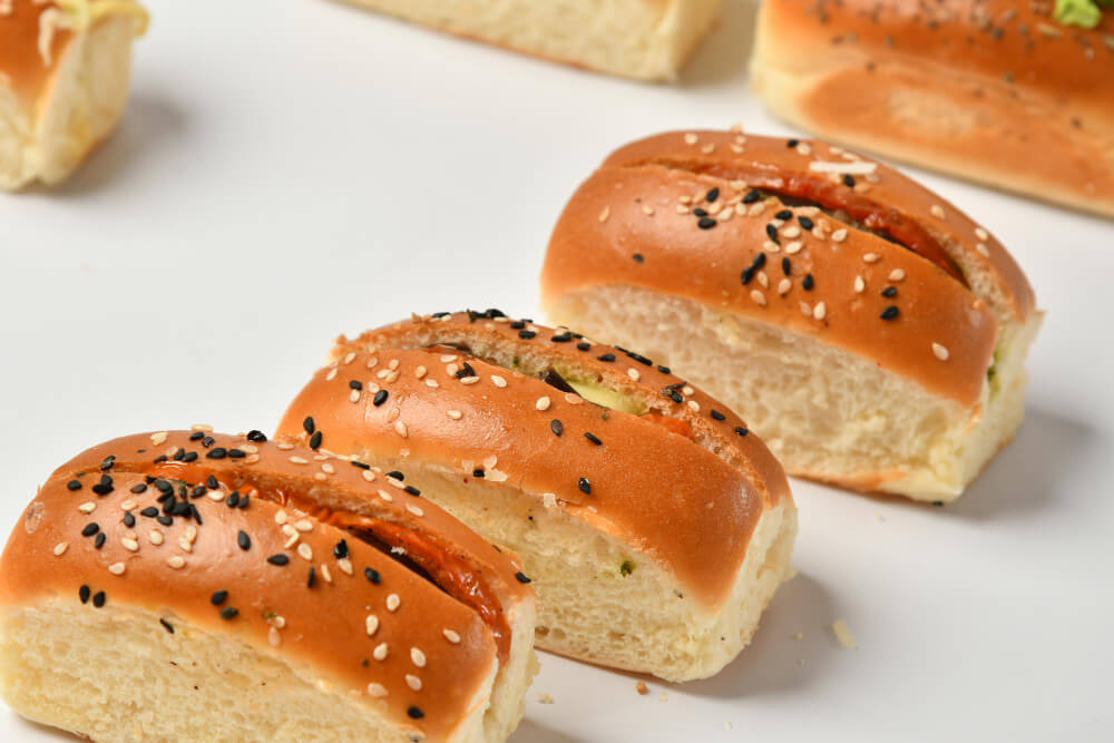 Soft, golden brown bread rolls topped with black and white sesame seeds, arranged on a white surface.