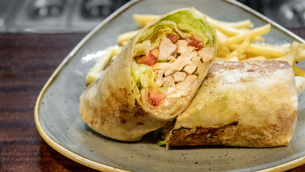 Chicken Caesar Wrap served on a plate with a side of French fries, showcasing fresh ingredients like lettuce, chicken, and tomatoes.