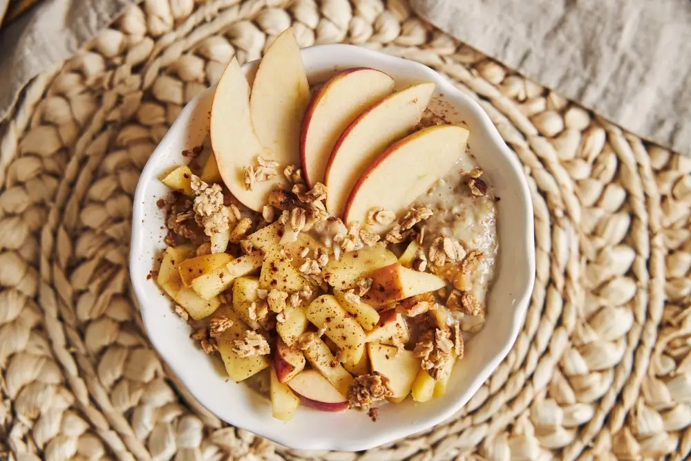 A bowl of fresh apple slices, diced apples, and granola served on a rustic woven placemat.