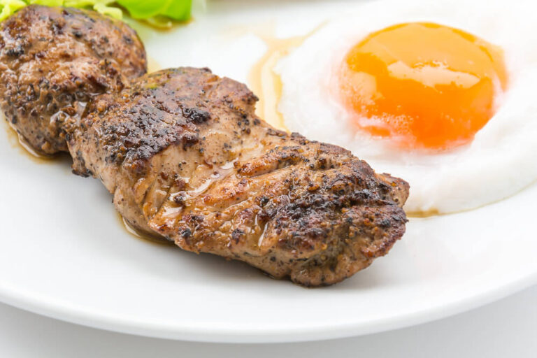 Juicy grilled steak with a sunny-side-up egg and fresh lettuce served on a white plate.