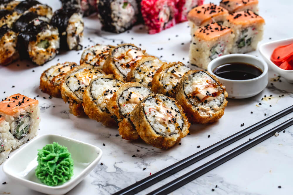 A platter of cooked sushi rolls including crispy tempura rolls, served with soy sauce, wasabi, and pickled ginger.