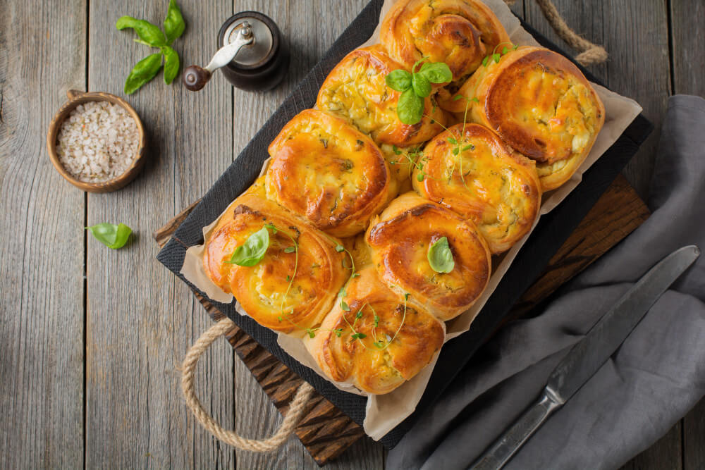 Golden pull apart garlic rolls topped with fresh herbs, served on a rustic wooden tray with salt and basil garnish.