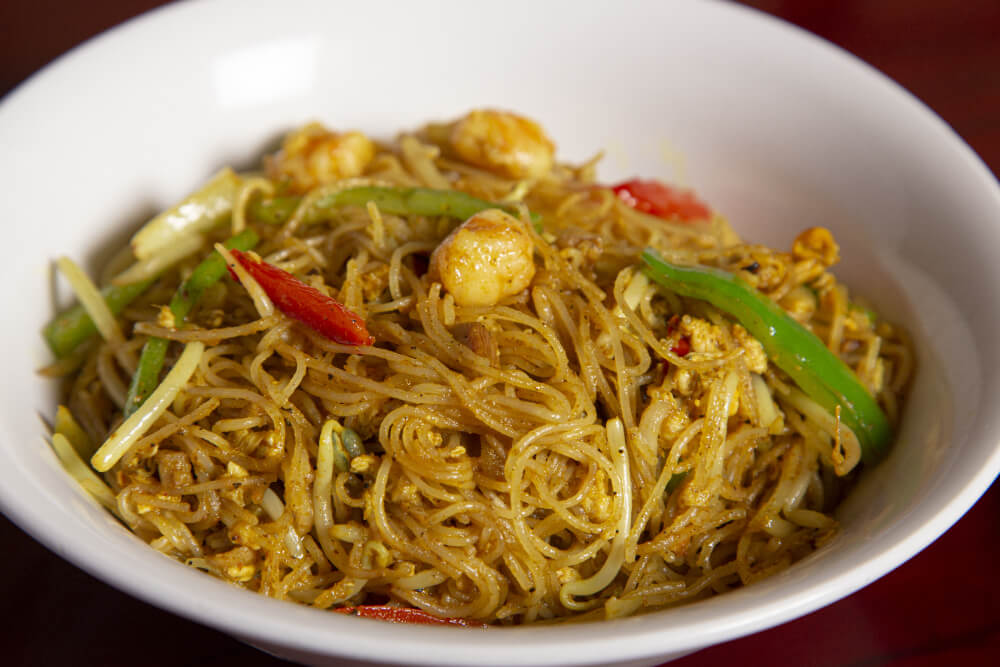 A bowl of stir-fried noodles with shrimp, vegetables, and a golden curry seasoning. A bowl of stir-fried noodles with shrimp, vegetables, and a golden curry seasoning.