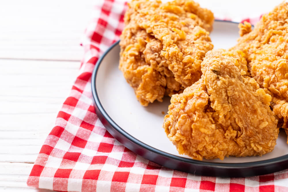 Crispy fried chicken pieces served on a white plate with a red and white checkered cloth.