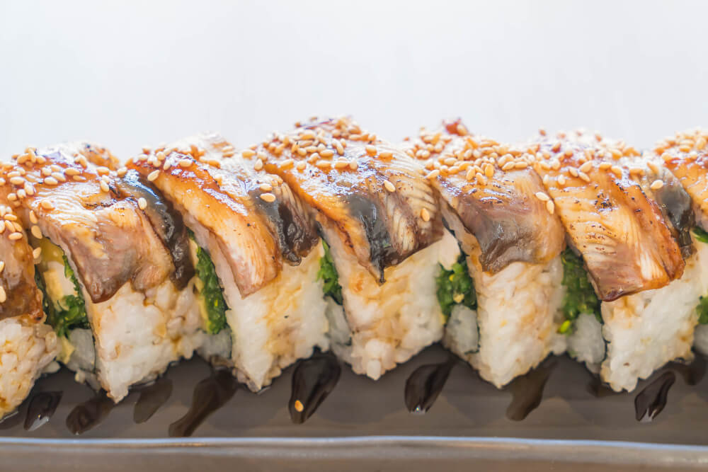 Close-up of cooked eel sushi rolls garnished with sesame seeds and served with a drizzle of sauce.