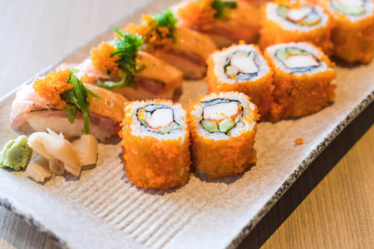 A plate of vibrant cooked sushi rolls with crab, avocado, and tobiko, served with wasabi and pickled ginger.