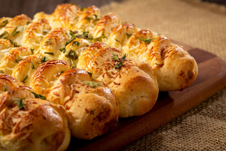 Golden brown pull apart garlic bread topped with melted cheese and fresh herbs on a wooden board.