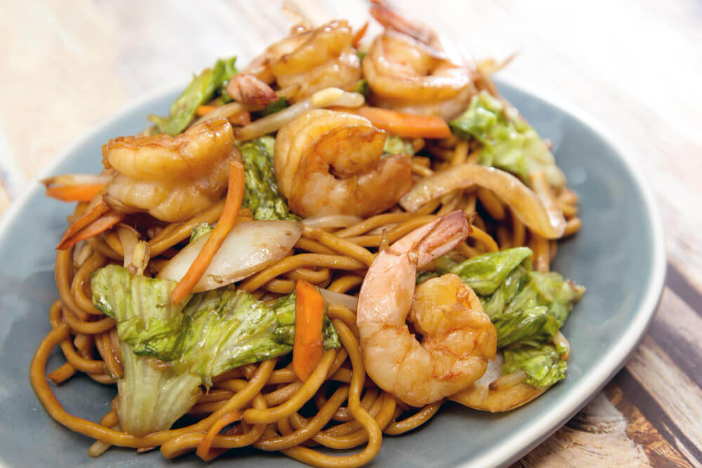 A plate of shrimp chow mein with crispy vegetables, golden noodles, and plump shrimp.