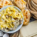 Plate of creamy chicken spaghetti carbonara with fresh pasta, eggs, and wheat in the background.