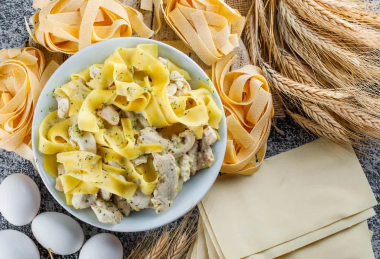 Plate of creamy chicken spaghetti carbonara with fresh pasta, eggs, and wheat in the background.