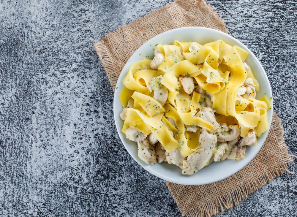 Top view of chicken spaghetti carbonara on a white plate with wide pasta ribbons served on a rustic burlap mat.