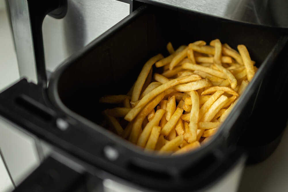 Golden French fries are freshly cooked in an air fryer basket, ready to serve.