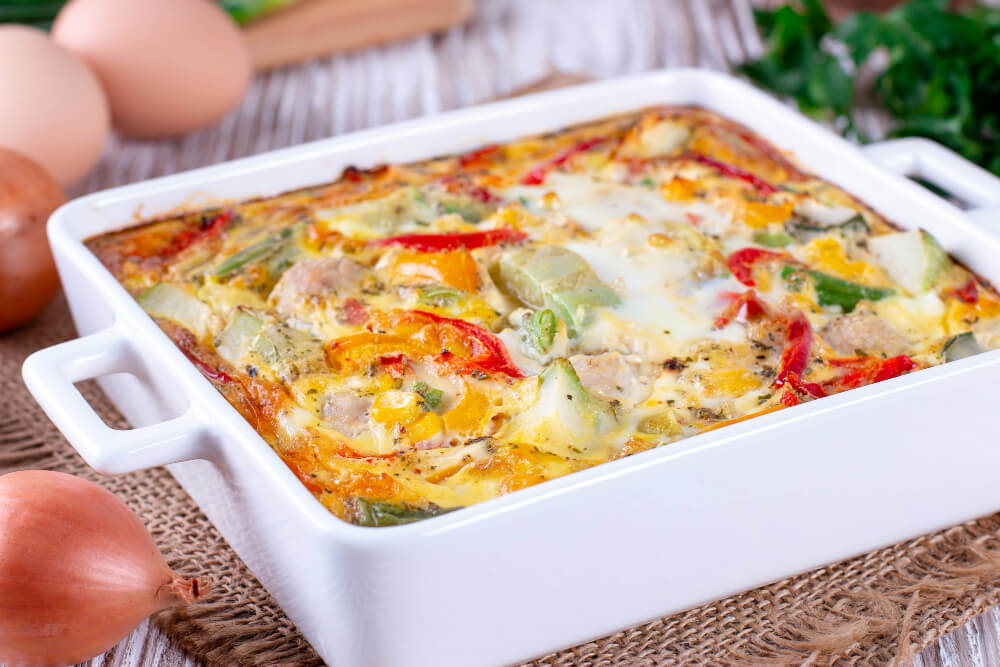 A freshly baked Eggs Benedict casserole filled with colorful vegetables like peppers and onions in a white casserole dish.