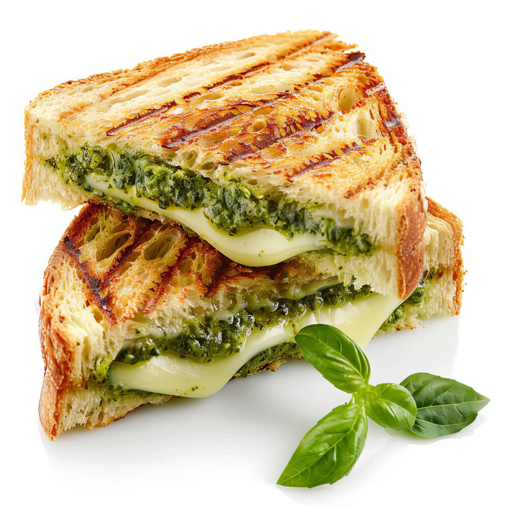 Grilled cheese sandwich with melted mozzarella and pesto sauce, sliced in half and garnished with fresh basil leaves on a white background