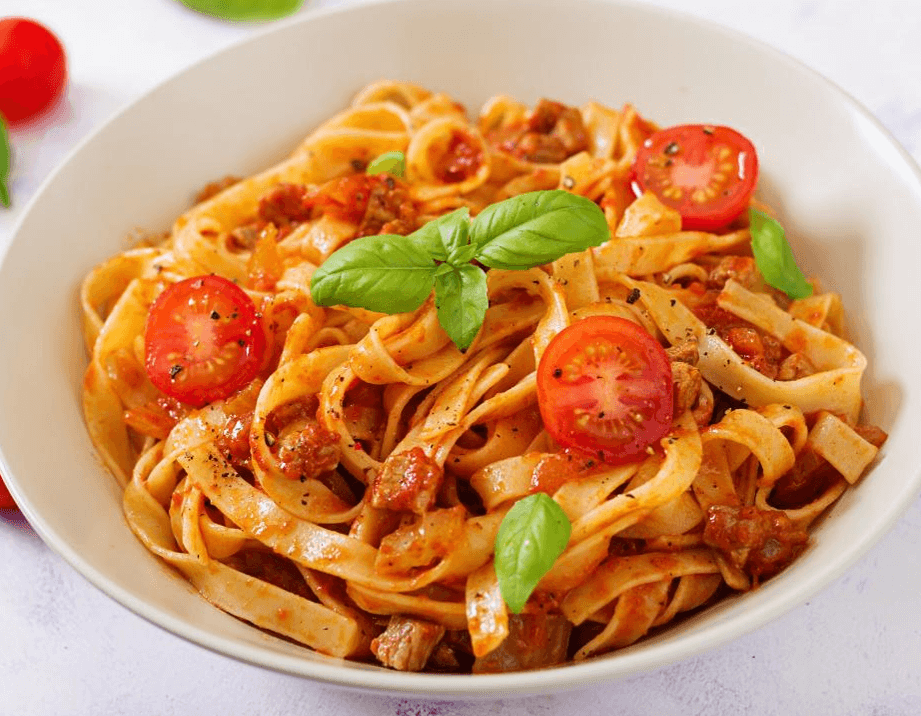 A hearty bowl of sausage ragu served over fettuccine, garnished with fresh parsley and grated Parmesan cheese.